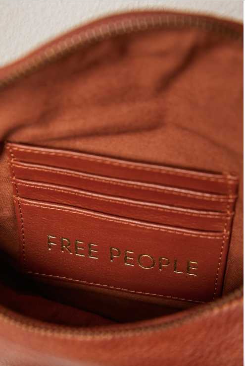 Free People Palmer Crossbody bag made from soft leather with a smooth, polished finish. This compact bag features an adjustable strap and a zippered main compartment, offering a stylish and functional accessory for everyday use, Spiced Rum