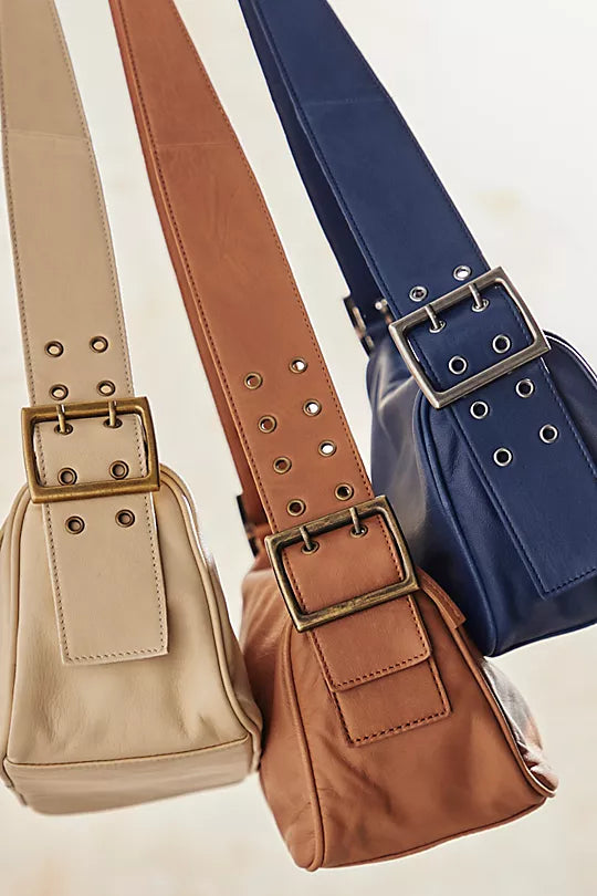 Free People Arm Candy Bag in luxe leather with a thick adjustable strap, rivet detailing, and a zip-top closure