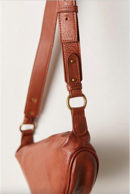 Free People Palmer Crossbody bag made from soft leather with a smooth, polished finish. This compact bag features an adjustable strap and a zippered main compartment, offering a stylish and functional accessory for everyday use, Spiced Rum