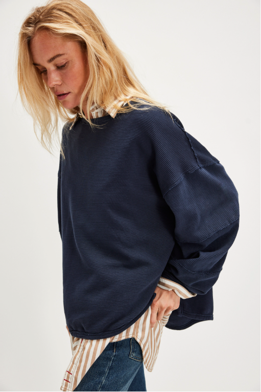 "We The Free Total Eclipse Tee" in an oversized, long-sleeve ribbed cotton fabric. The shirt features a wide scoop neckline, dropped shoulders, and exposed raw seams, Deeper Iris